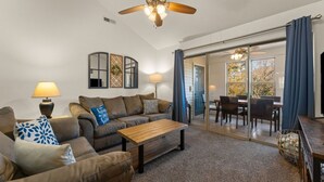 A living room with a sofa, coffee table, and a ceiling fan. There is a sliding glass door leading to an outdoor dining area. - Luxury Lake Vacation at Emerald Pointe (Hollister)