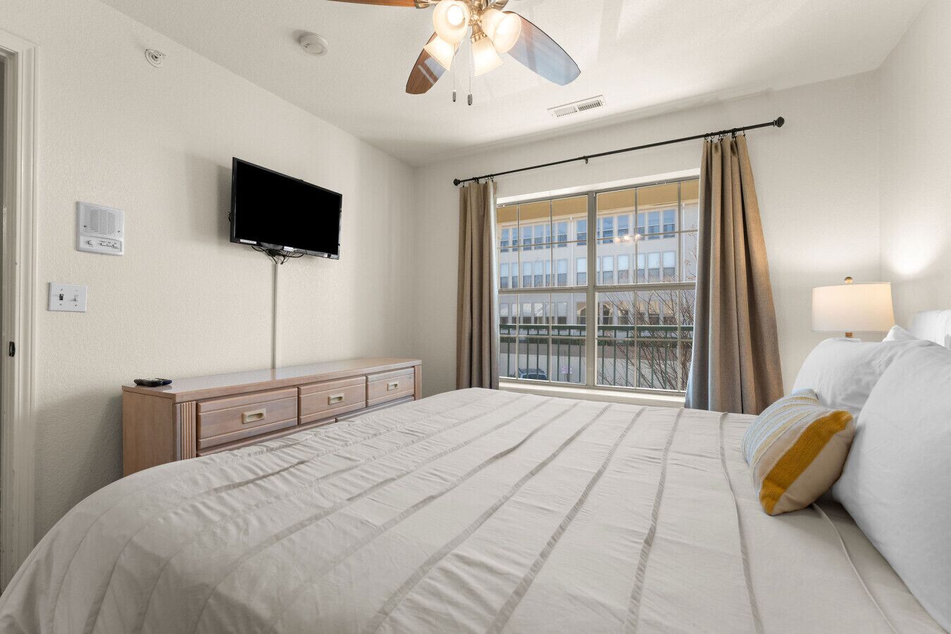 Hotelkamer met een bed, een televisie, een plafondventilator, een raam met gordijnen en een dressoir.