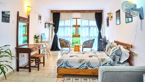 Ein Schlafzimmer mit Bett, Schreibtisch, Stühlen und einem großen Fenster mit Vorhängen.