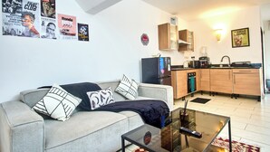 Ein Wohnzimmer mit einer Couch, einem Couchtisch und einer Küchenzeile mit Schränken und Geräten.
