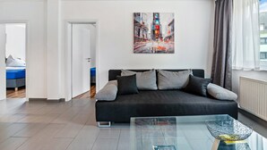 A modern living room with a black sofa, a glass coffee table, and a cityscape painting on the wall. - Ideal for Contractors: 2 Bedrooms for 4 Guests (65 m²) in Saarbrücken, Free Parking (Saarbrücken)