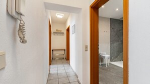 Un couloir avec un mur blanc, une porte donnant sur une salle de bain et une pancarte « Accueil » sur le mur.