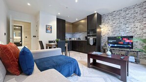 Ein modernes Wohnzimmer mit einer Couch, einem Couchtisch, einem Fernseher und einer Küche im Hintergrund.