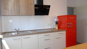 Eine Küche mit weißen Schränken, einer Edelstahl-Spüle, einem roten Kühlschrank und einer schwarzen Dunstabzugshaube.