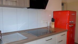 Une cuisine moderne avec des meubles blancs, un réfrigérateur rouge et une cuisinière encastrée.