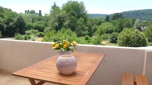 Un balcon avec une table en bois et un vase rempli de fleurs jaunes.