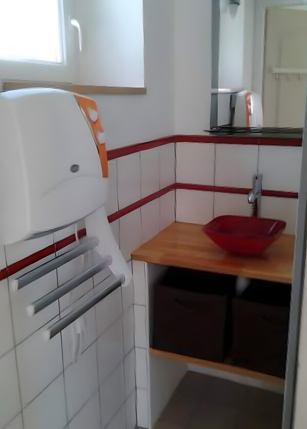 A compact kitchenette with a white tiled backsplash, a wooden countertop, a red bowl, and a built-in oven.