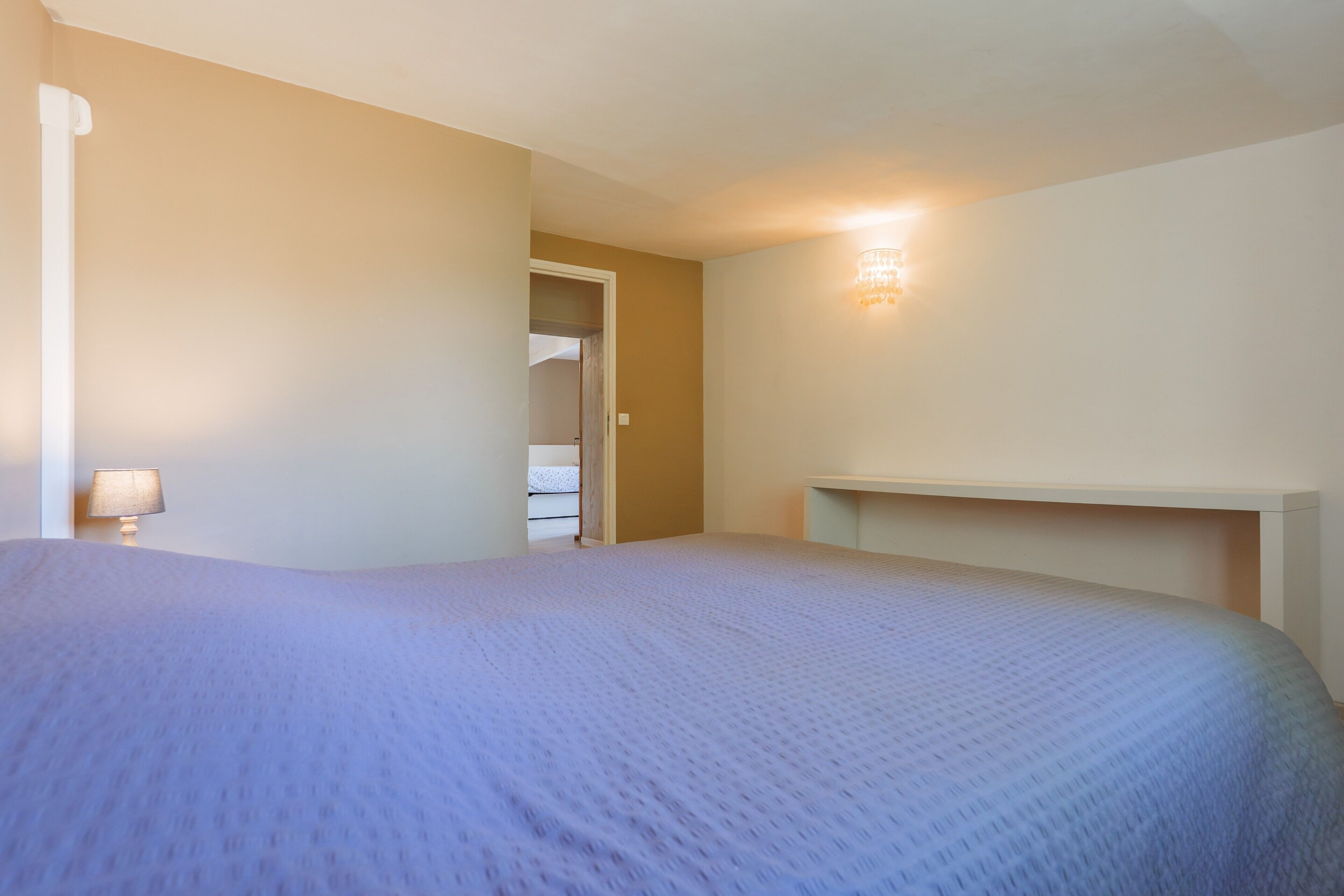 A bedroom with a bed, a nightstand, a wall-mounted light, and a door leading to a closet.