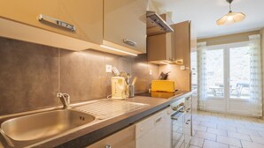 A modern kitchen with a sink, countertop, and cabinets. There is a window with curtains and a view outside.