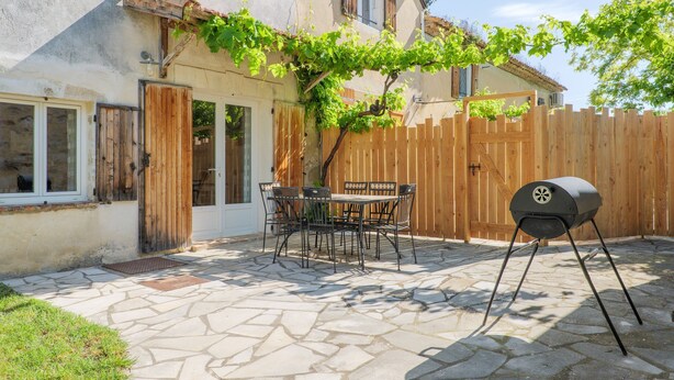 A patio with stone flooring, a wooden fence, a table with chairs, and a barbecue grill.