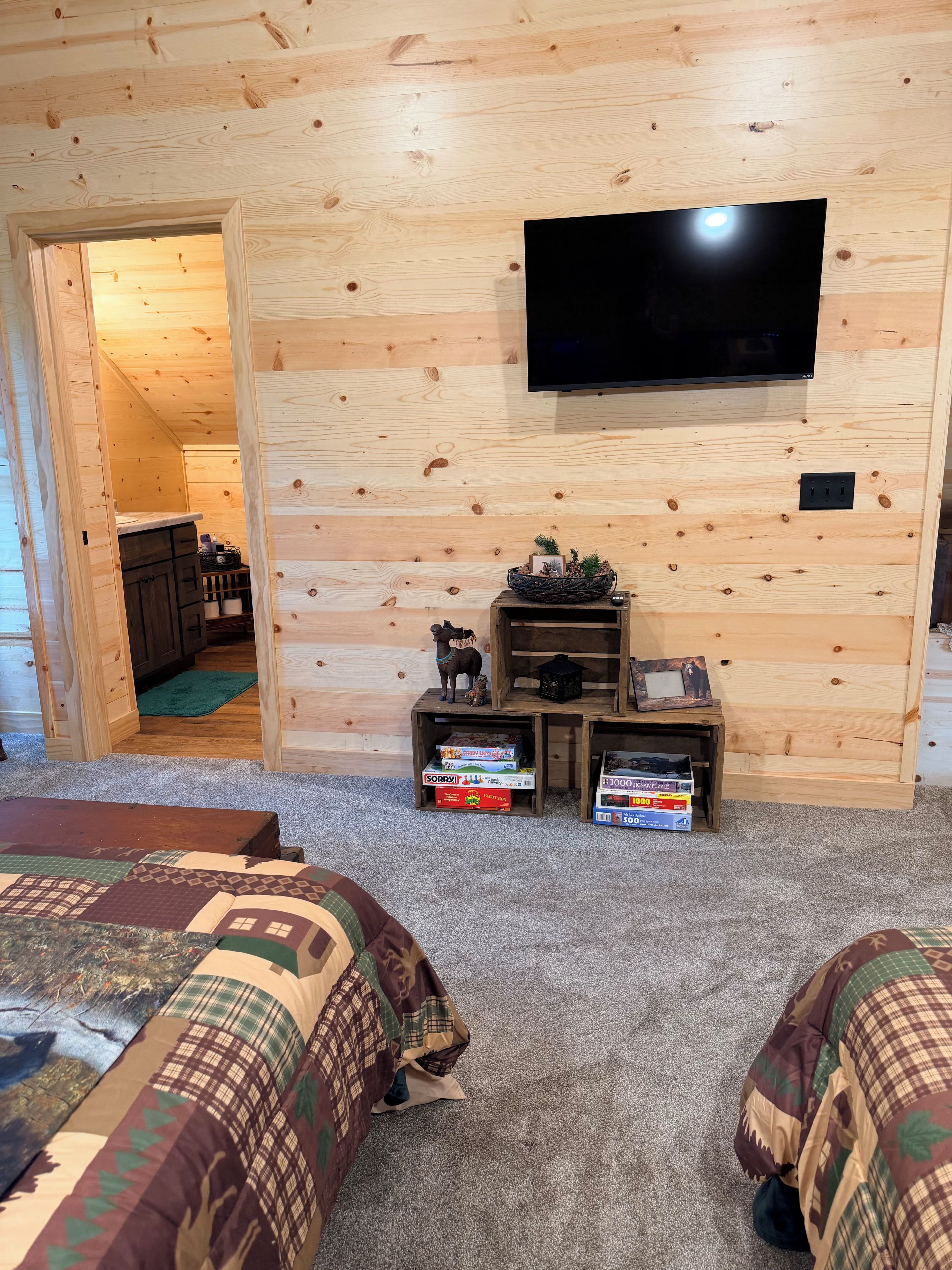 A room with two beds, a television mounted on the wall, and a small wooden shelf with items.