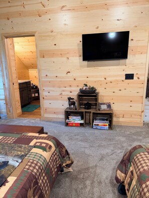 A room with two beds, a television mounted on the wall, and a small wooden shelf with items.