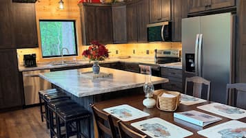 A modern kitchen with wooden cabinets, a stainless steel refrigerator, and a large window.