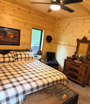 A wooden cabin bedroom with a bed, dresser, chair, and a ceiling fan.