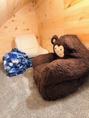 A cozy room with a plush brown teddy bear, a white pillow, and a blue patterned blanket on a carpeted floor.