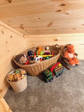 A wooden play area with a basket of toys, a toy truck, and a stuffed animal.