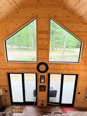 A wooden interior with a large clock, two windows, and a door leading outside.
