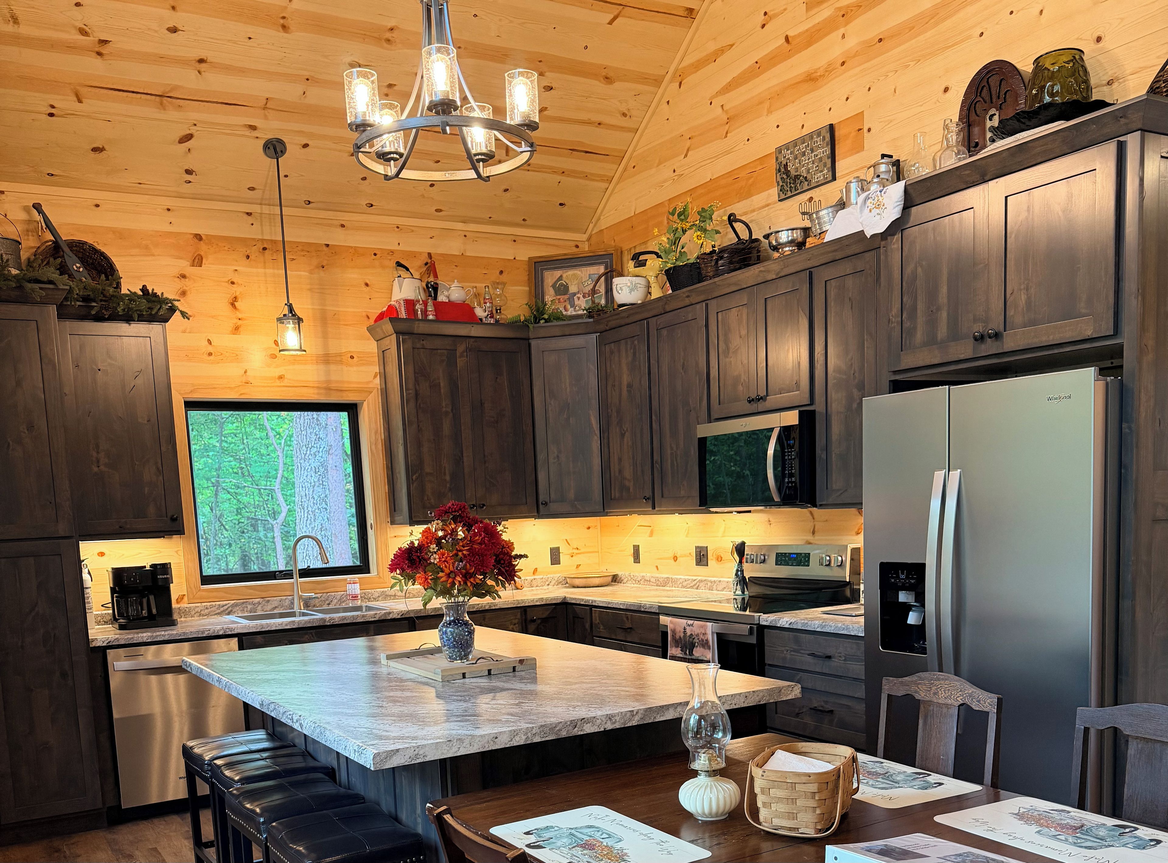 Una cocina moderna con armarios de madera oscura, electrodomésticos de acero inoxidable, una isla grande con un florero y vistas al exterior a través de una ventana.