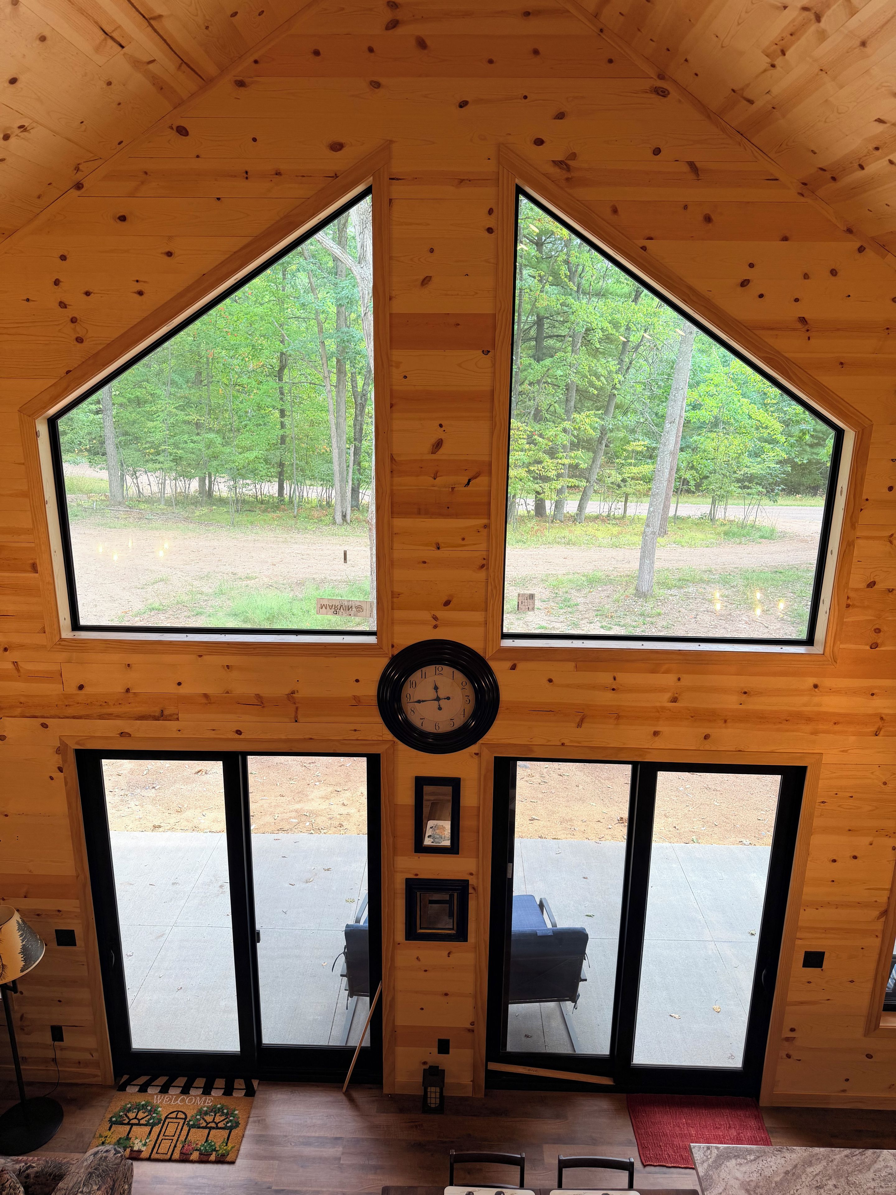 Un intérieur en bois avec une grande horloge, deux fenêtres et une porte donnant sur l’extérieur.