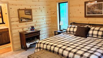 Quarto de cabana de madeira com cama, mesa de cabeceira, cômoda, ventilador de teto e janela.