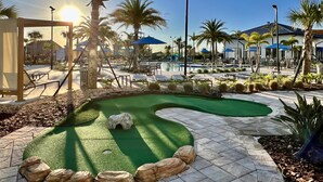 Een putting green omringd door palmbomen en een zwembad.