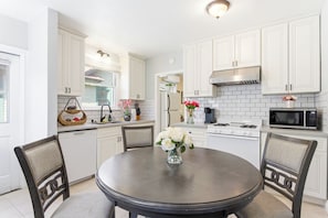 A kitchen with white cabinets, a stove, a microwave, and a dining table with chairs. - Private Detached Bungalow in Prime Pasadena King Bed Peaceful & Central! (Pasadena)