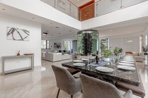 A spacious dining area with a long table set for a meal, a kitchen in the background, and a large decorative water feature.