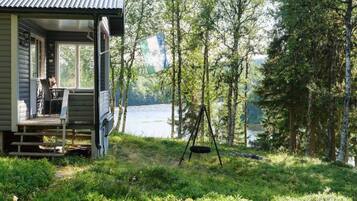 A cabin with a porch, a swing, and a view of a lake surrounded by trees.