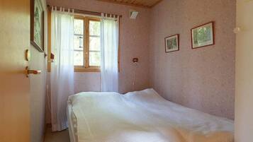 Ein Schlafzimmer mit einem Einzelbett, einem Fenster mit Vorhängen und zwei gerahmten Bildern an der Wand.