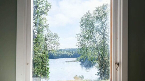 Vista pela janela de um lago com árvores, um prato de pães em um parapeito.