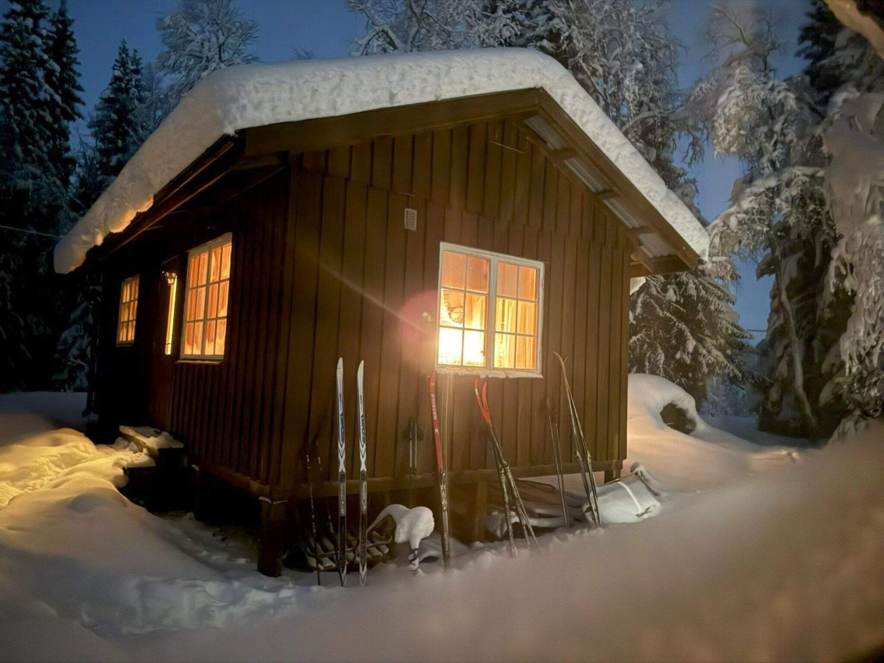 A wooden cabin with a snow-covered roof, windows, and a chimney.