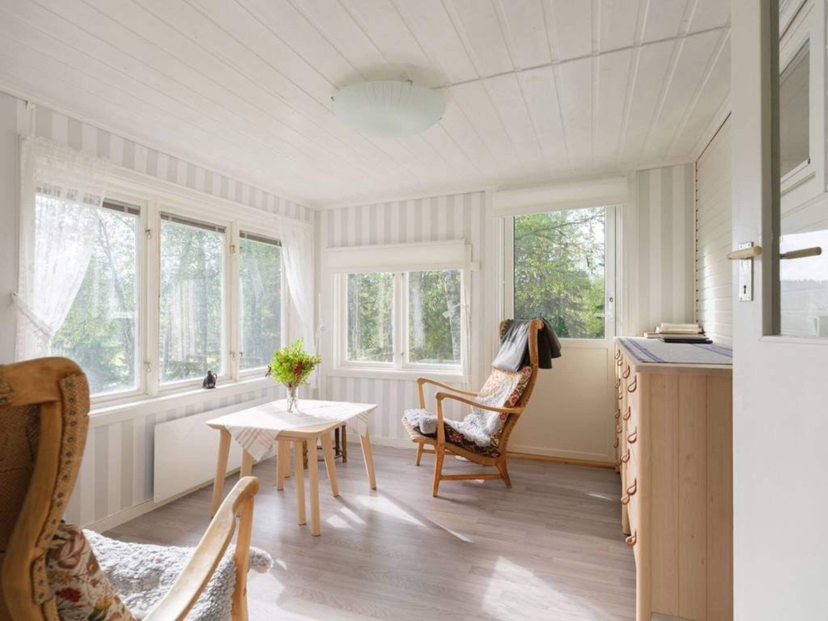 A room with a dining table, chairs, a window with curtains, a wooden chair with a blanket, and a radiator.