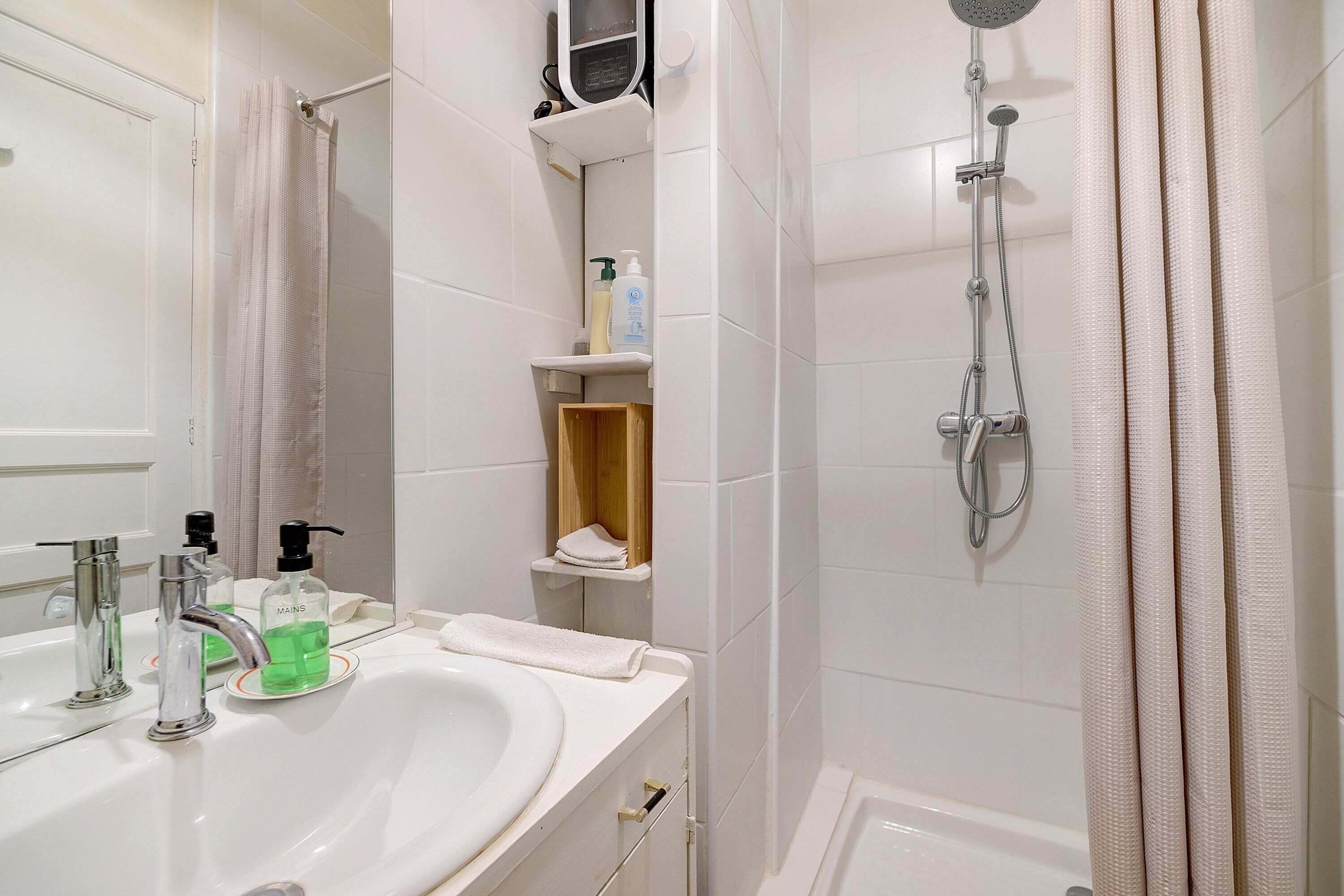 A bathroom with a sink, mirror, shower, and storage shelves.