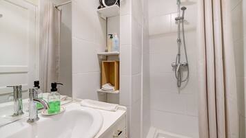 A bathroom with a sink, mirror, shower, and storage shelves.