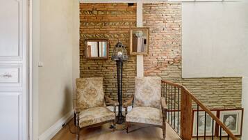A room with a brick wall, two patterned chairs, a floor lamp, and a staircase.