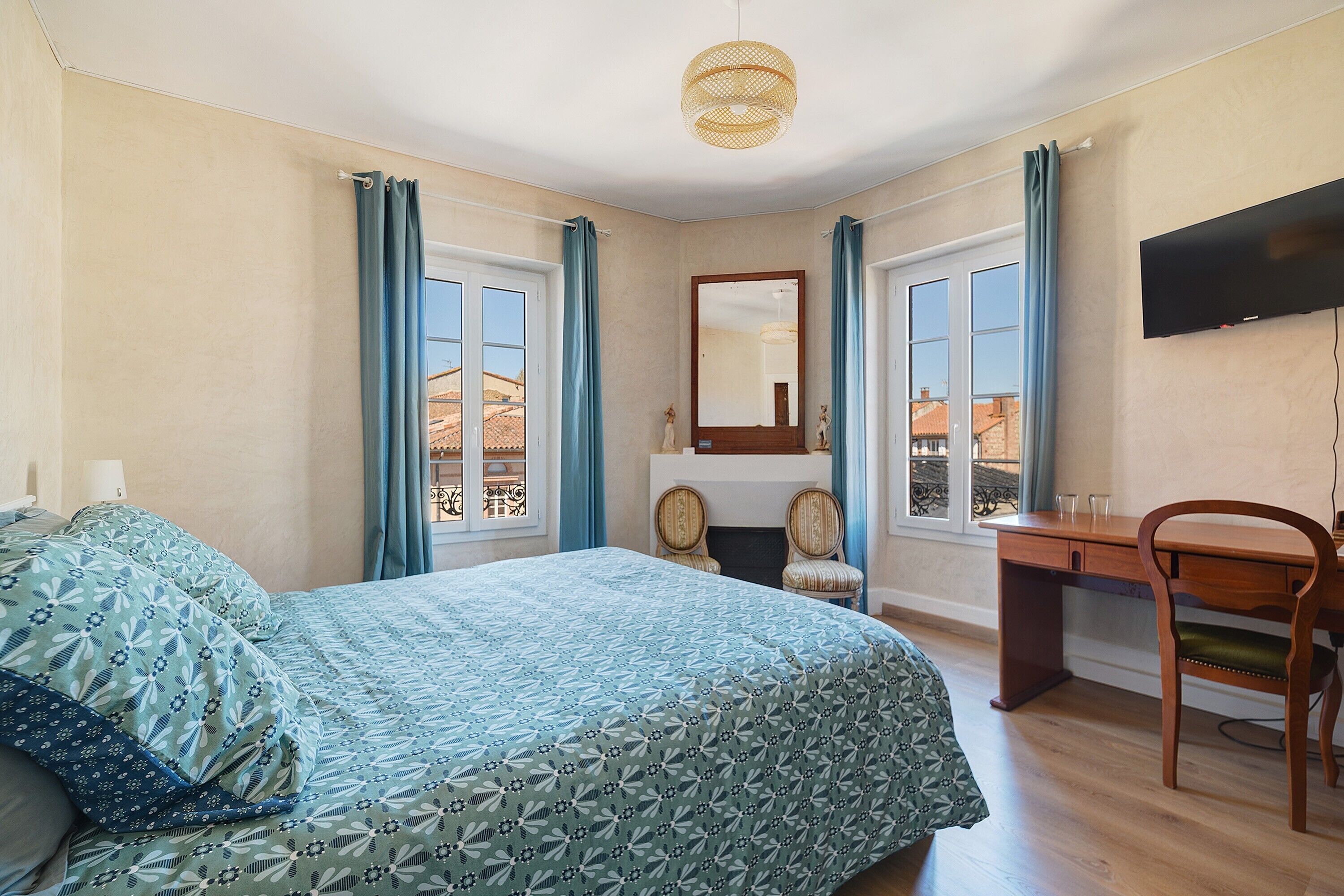 A bedroom with a bed, a desk, a chair, a television, and a window with curtains.