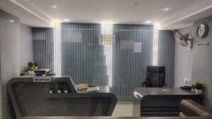 Un comptoir d’accueil avec un panneau, une horloge, un ventilateur et un mur avec des stores verticaux.