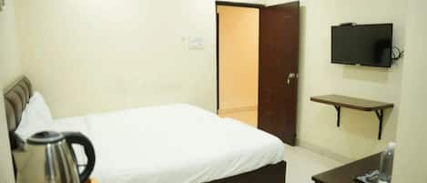 Une chambre d’hôtel avec un lit, un téléviseur fixé au mur, une petite table avec une bouilloire et une porte donnant sur une autre pièce.