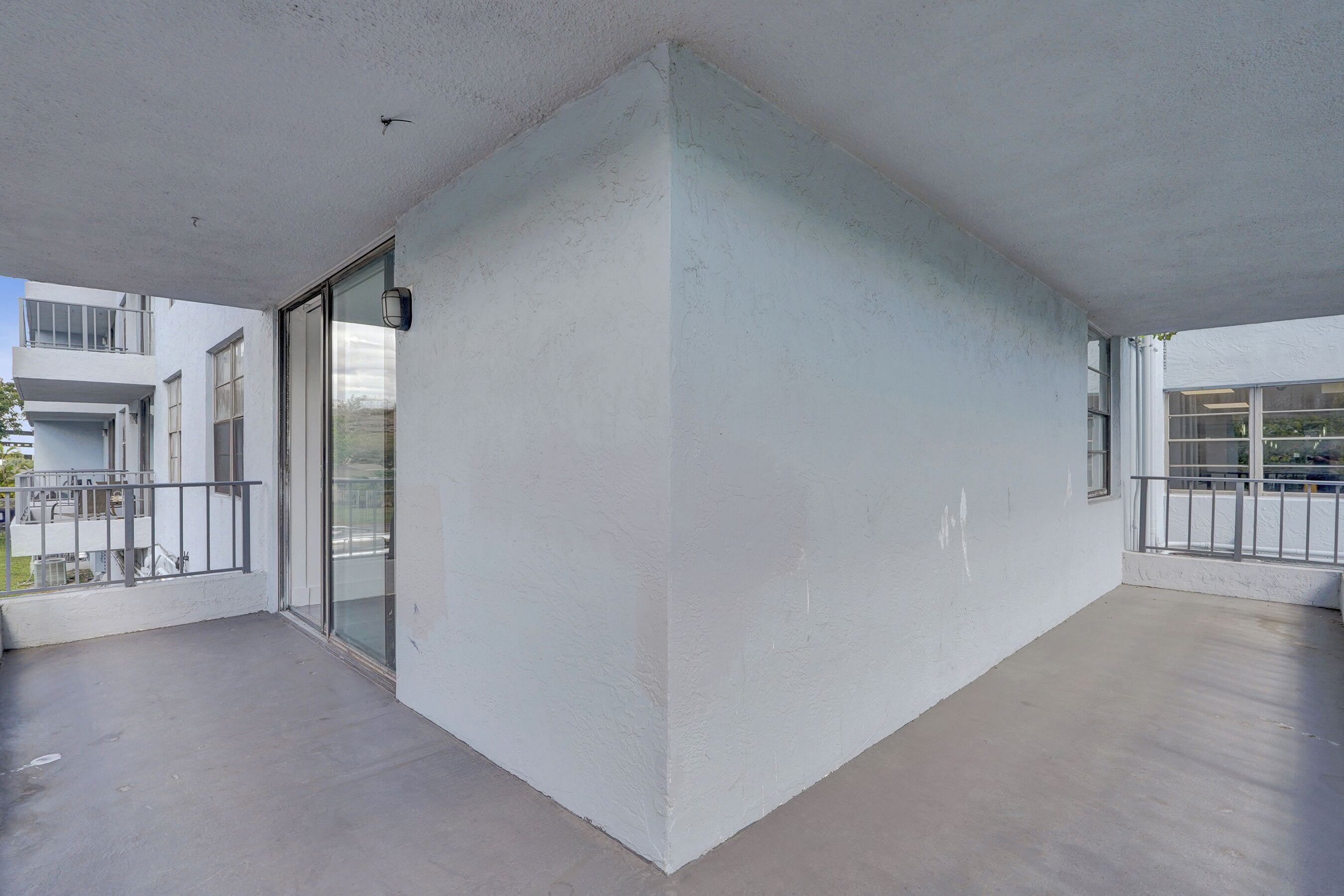 Esquina de un edificio moderno con balcón, puerta de cristal y pared blanca.