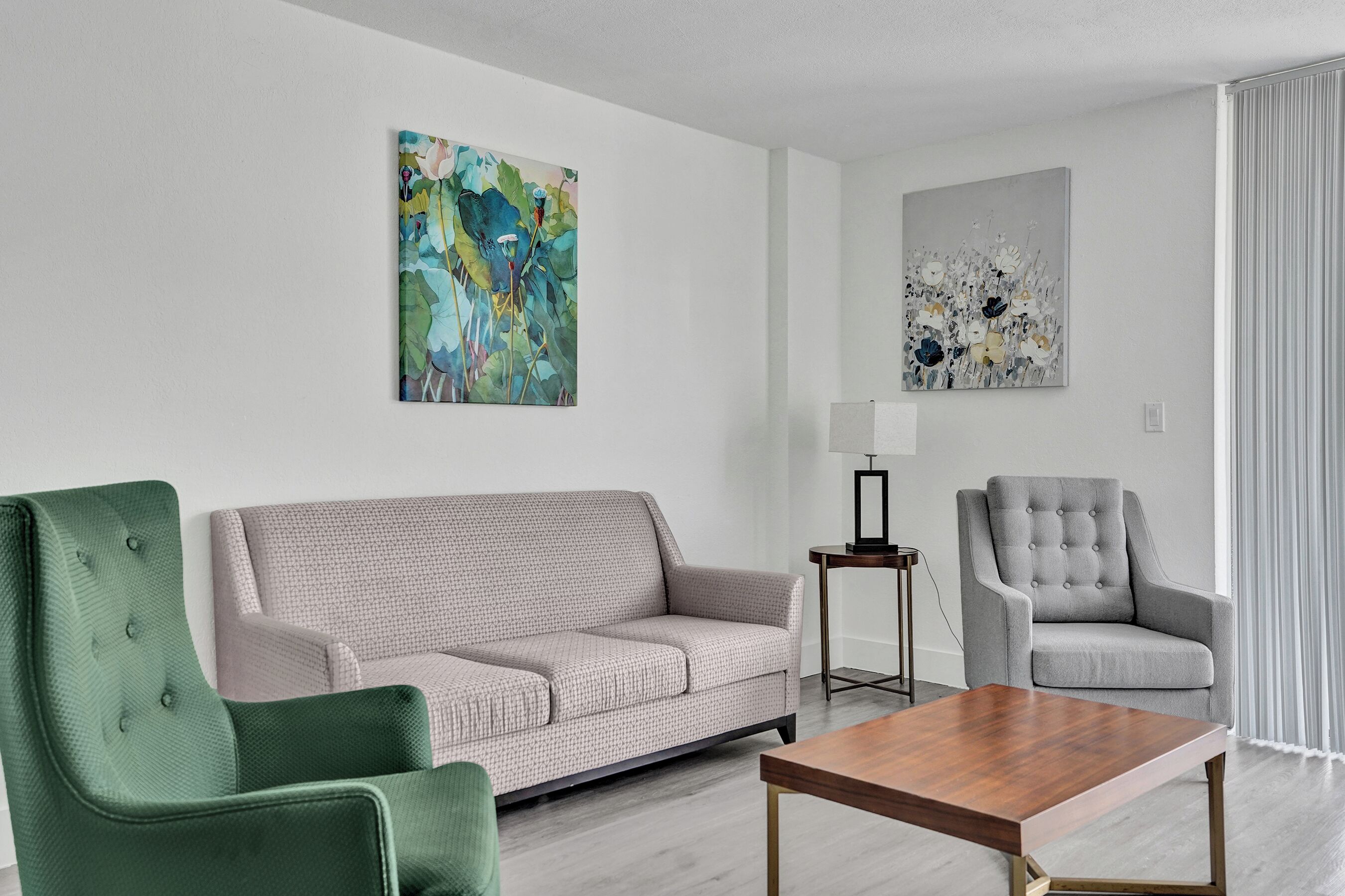 A modern living room with a sofa, two armchairs, a coffee table, and two abstract paintings on the walls.