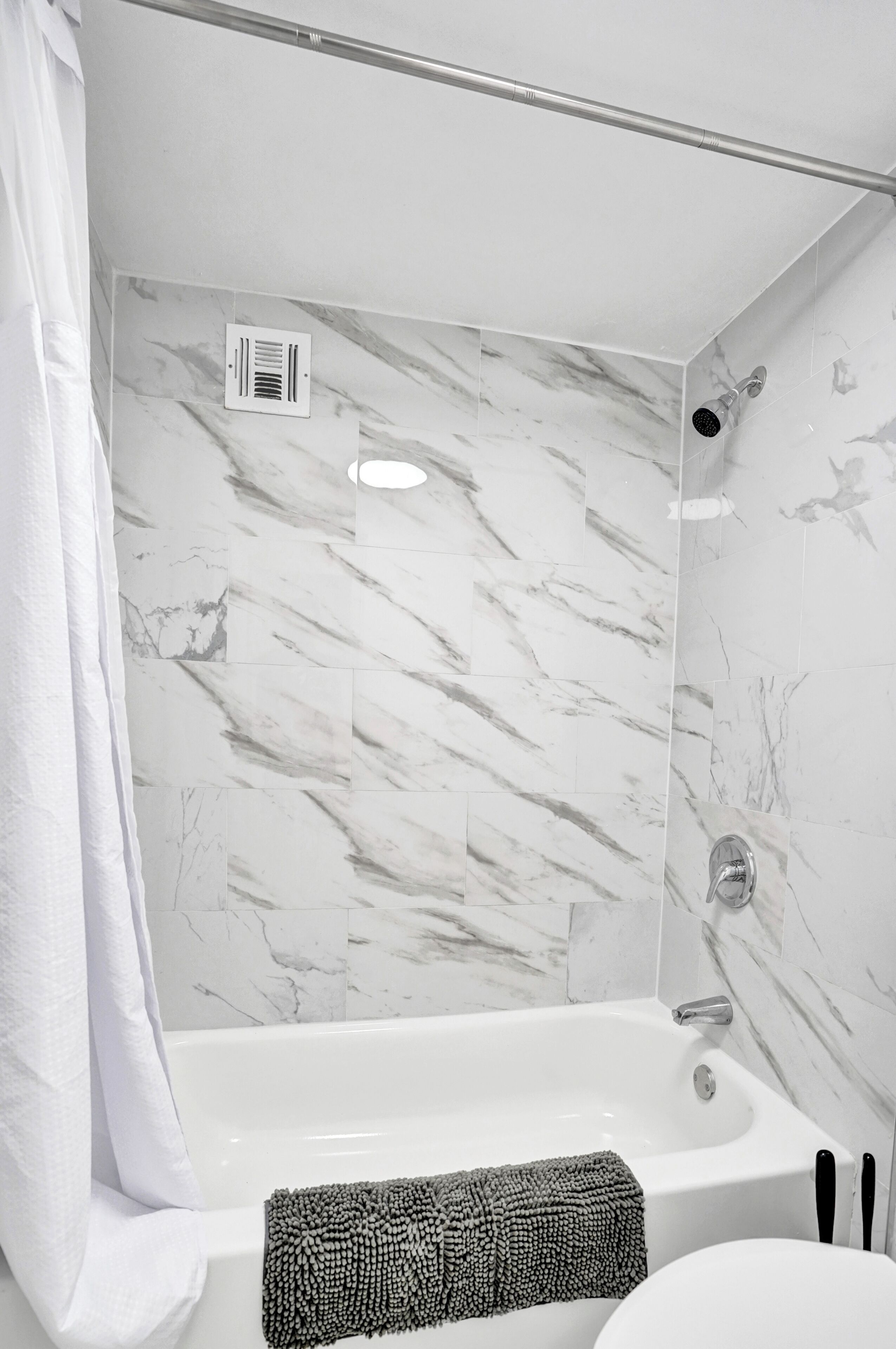 A bathroom with a white bathtub, a showerhead, and a towel rack.