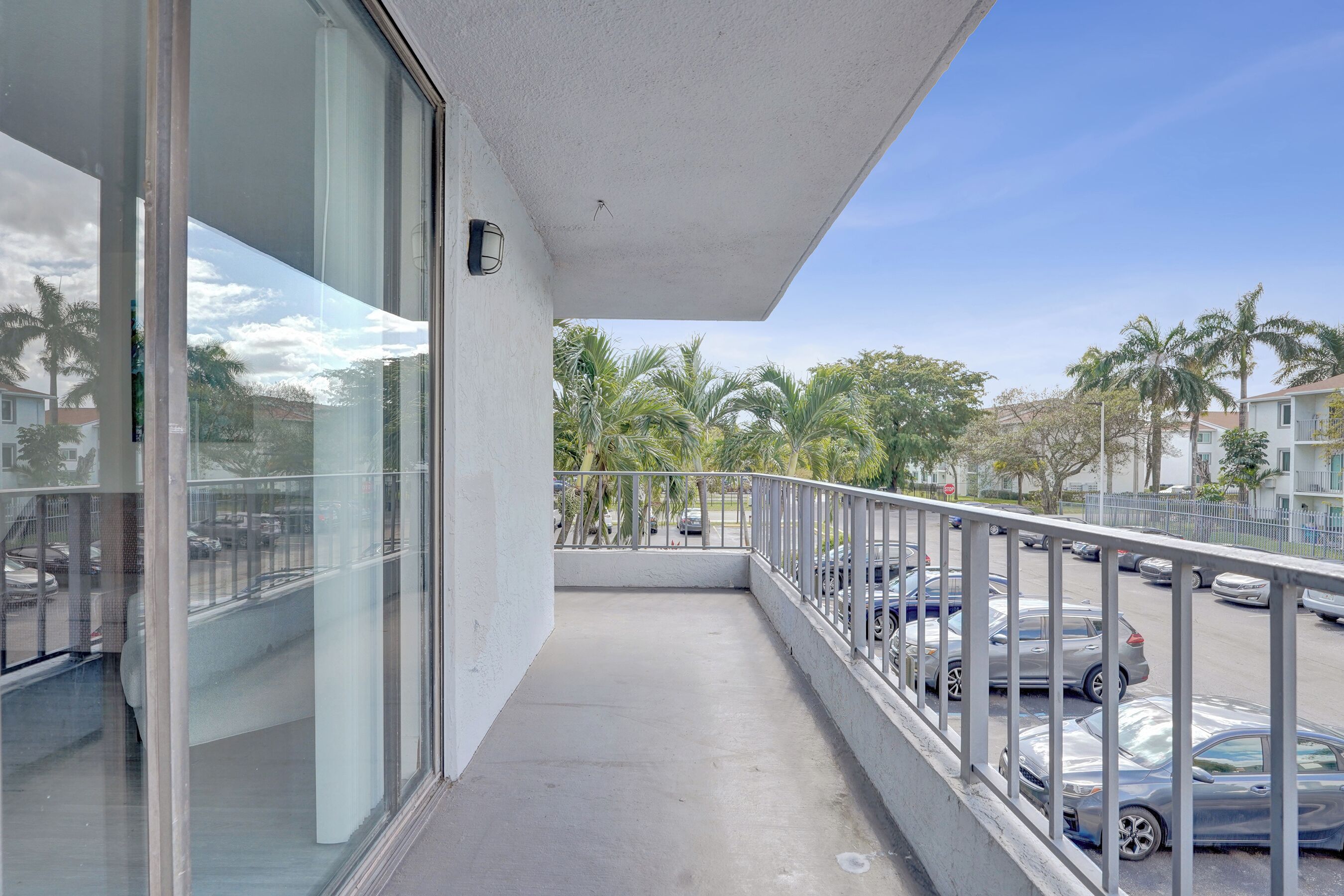 A balcony with a view of parked cars and palm trees.