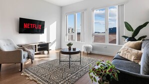 A modern living room with a flat-screen TV, a sofa, a chair, a coffee table, and a large window with a view. - Light-Filled Artsy Stay in Little Tokyo (Los Angeles)