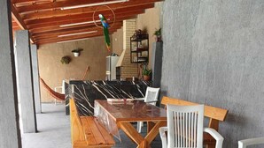 Terrassa exterior amb taula i cadires de fusta, un hamaca i un lloro.