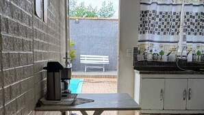Cuina petita amb sòl de rajola, taula baixa amb un tamboret i finestra amb vista a un pati.