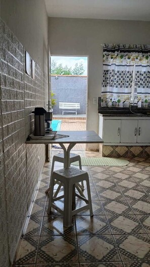 Una cocina estrecha con suelo de baldosas, una pequeña mesa con un taburete y un ventanal con vistas a un patio.