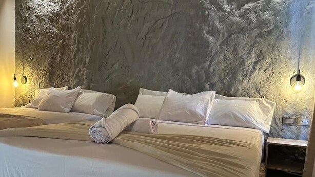 Une chambre avec un mur en pierre, deux lits et des lampes fixées au mur.