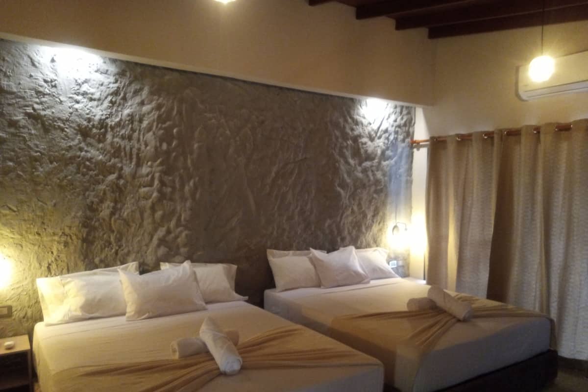 Habitació d'hotel amb dos llits, una paret amb relleu, una cortina i una petita taula de nit amb una làmpada.