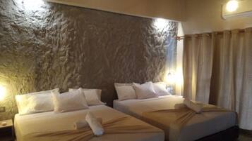 Habitación de hotel con dos camas, una pared texturizada, una cortina y una mesita de noche con lámpara.