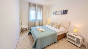 Ein Schlafzimmer mit einem Bett, einem Nachttisch, einem Sessel und einem Fenster mit Vorhängen.